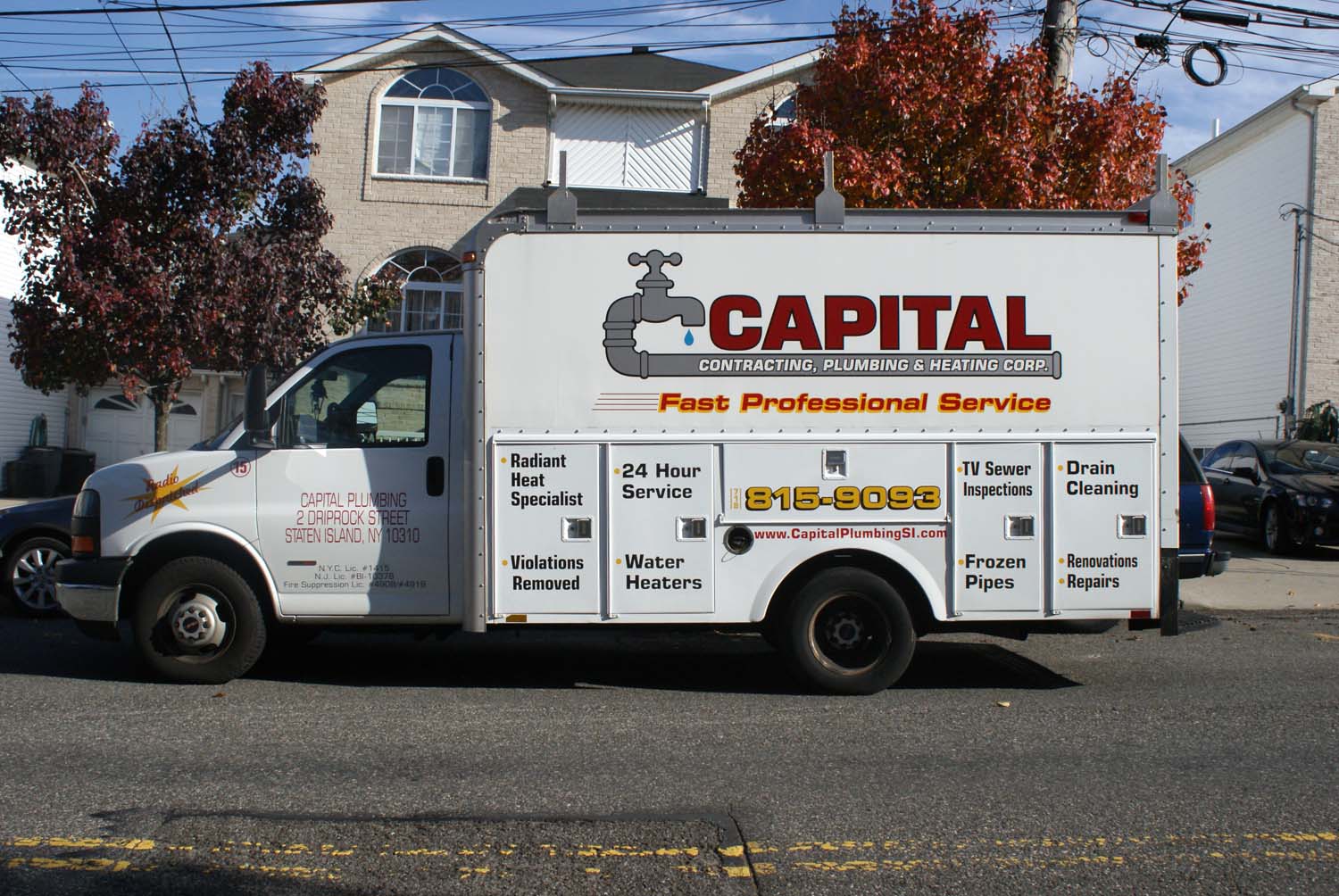 Service truck beside autumn foliage on a residential street.
